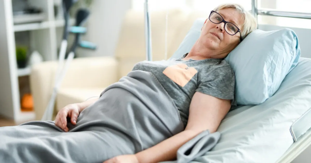 Older female patient lying in a hospital bed with a light gray blanket, recovering from hip fracture surgery, with underarm crutches nearby.