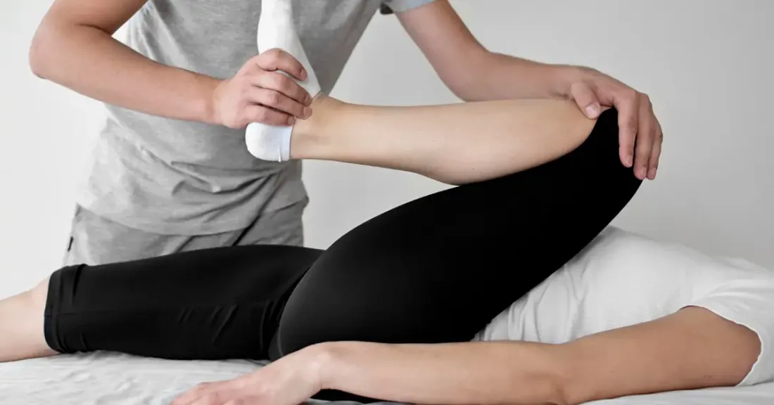 Physiotherapist guiding passive hip flexion stretch with sock assist during early post-hip arthroscopy rehab