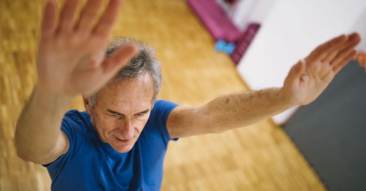 Senior man performing active shoulder elevation exercises in gym during Phase II-III recovery after reverse total shoulder arthroplasty.