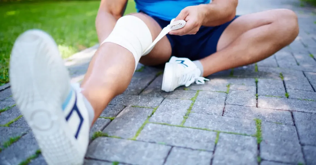 An athlete wrapping a compression bandage around their knee and upper shin area during recovery from proximal tibia fracture surgery.