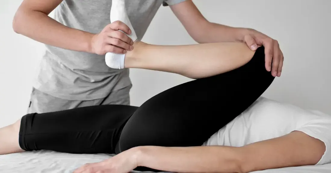 Physiotherapist guiding passive hip flexion stretch with sock assist during early post-hip arthroscopy rehab